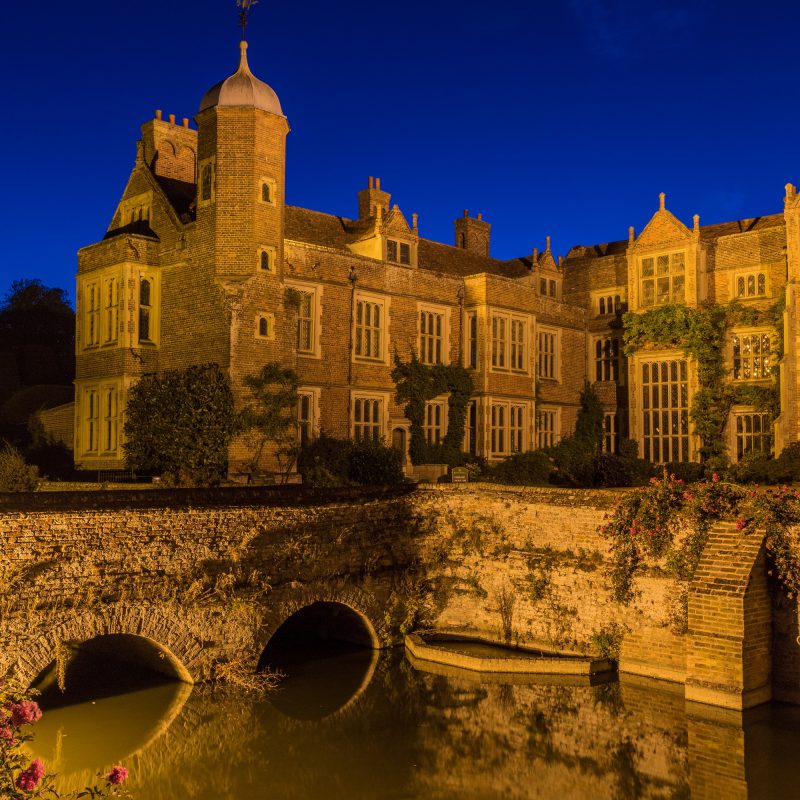 Kentwell Hall seen at floodlit at night with surrounding moat